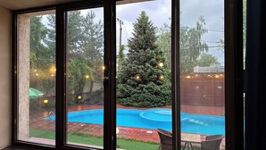 A room with a large sliding glass door leading to a backyard with a swimming pool, a Christmas tree, and outdoor lighting. - Gatsby Ortosay (Bishkek)