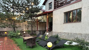 A patio with outdoor furniture, a stone wall, and string lights. - Gatsby Ortosay (Bishkek)