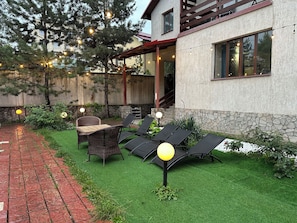 Un patio con mobiliario exterior, una pared de piedra y luces colgantes.