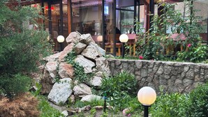 A stone wall with greenery, a wooden structure with glass doors, and outdoor seating. - Gatsby Ortosay (Bishkek)
