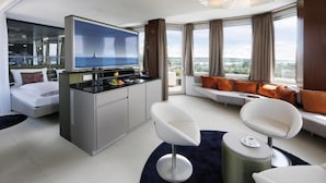 A modern hotel room with a TV, seating area, and a view of the city. - aquaTurm Hotel GmbH (Radolfzell am Bodensee)