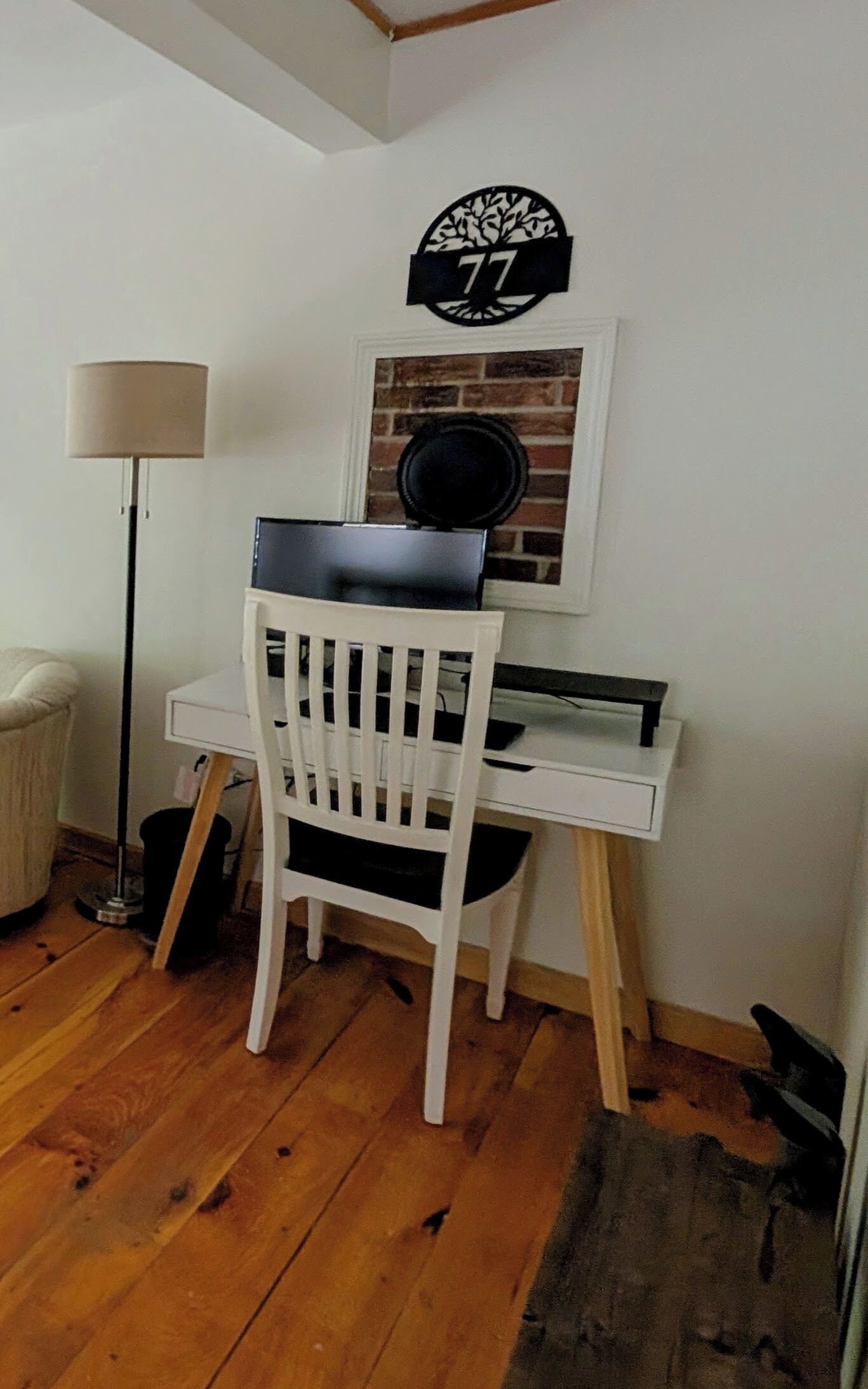 Une pièce de taille modeste, avec un bureau blanc, une chaise, une lampe et un élément décoratif fixé au mur.