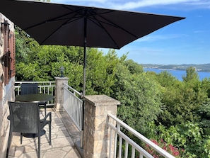 A patio with a table and chairs, a large umbrella, and a view of the sea. - Villa Carlotta | Sea view, pool & large terrace above Viganj (Kuciste)