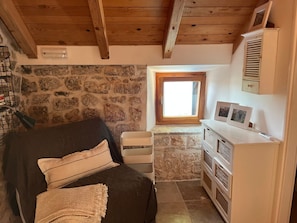 A cozy room with a stone wall, a wooden ceiling, a window, a sofa, a small table, and a cabinet.