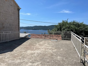 A terrace with a view of a lake, stone walls, and a metal railing.