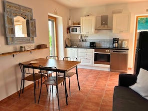 A compact kitchen with white cabinets, a microwave, a stove, and a refrigerator. There is a wooden dining table with chairs and a black sofa. - Villa Carlotta | Sea view, pool & large terrace above Viganj (Kuciste)