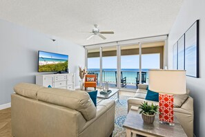 Ein Wohnzimmer mit einer Couch, einem Couchtisch, einem Fernseher und einem Balkon mit Meerblick.