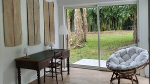Une pièce avec un plancher en bois, une table à manger entourée de chaises, un luminaire suspendu et une vue sur un jardin, visible à travers une porte vitrée.