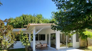 Une terrasse couverte avec une table et des chaises, une porte-fenêtre et une vue sur une maison en arrière-plan.