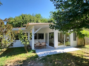 A covered patio with a table and chairs, a glass door entrance, and a view of a house in the background. - Charming stone house with swimming pool. Pets welcome! (Madaillan)