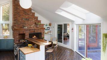 A kitchen with a brick wall, a stove, and a dining area with chairs.