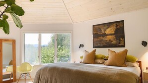 A bedroom with a large bed, a window with a view of greenery, a painting on the wall, and a plant hanging from the ceiling. - Serene 4-bedroom family friendly house perfect for your Stowe getaway (Stowe)