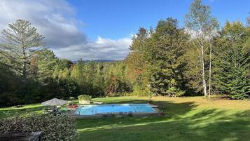 Ein Garten mit Schwimmbad, umgeben von Bäumen und einer Rasenfläche.