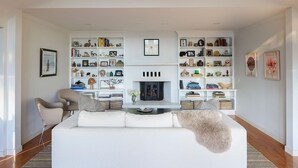 A modern living room with a white sofa, a fireplace, and built-in bookshelves filled with books and decorative items. - Serene 4-bedroom family friendly house perfect for your Stowe getaway (Stowe)