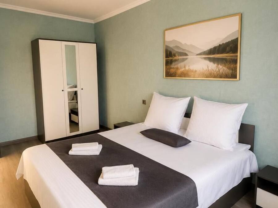 Una habitación de hotel con cama, armario, un cuadro y una lámpara en el techo.