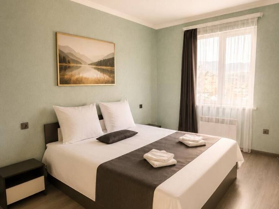 Una habitación de hotel con cama, mesita de noche, ventana con cortinas y una lámpara en el techo.