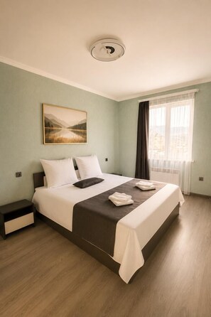 A hotel room with a bed, a nightstand, a window with curtains, and a ceiling light. - Luxury Unique Retreat in Armenia (Vanadzor)