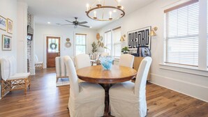 A dining area with a round wooden table, white upholstered chairs, a chandelier, and a ceiling fan. - The Ole Miss Square 3BR by Velvet Ditch Villas (Oxford)