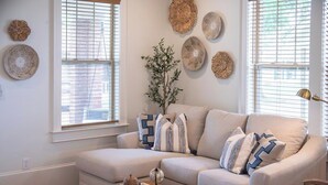 A living room with a beige sofa, decorative wall art, a potted plant, and a coffee table. - The Ole Miss Square 3BR by Velvet Ditch Villas (Oxford)
