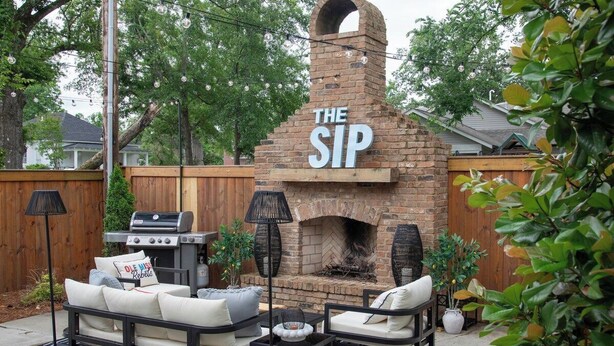 An outdoor patio with a brick fireplace labeled 'THE SIP,' a grill, and outdoor seating. - The Ole Miss Square 3BR by Velvet Ditch Villas (Oxford)