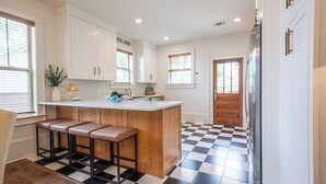 A kitchen with white cabinets, a wooden island with stools, a refrigerator, and a checkered floor. - The Ole Miss Square 3BR by Velvet Ditch Villas (Oxford)