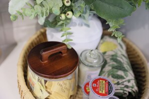 Una cesta de mimbre que contiene un tarro etiquetado 'The Earl Grey Tea', un frasco con etiqueta y un pequeño recipiente con etiqueta roja y blanca.