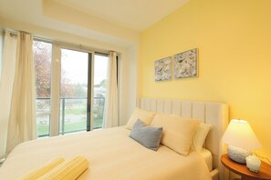 Una habitación de hotel con una cama grande, una lámpara de noche, una ventana con cortinas y dos obras de arte colgadas en la pared.