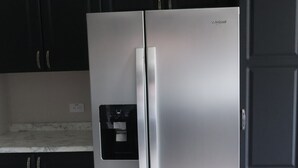 Un refrigerador Whirlpool de acero inoxidable en una cocina con gabinetes oscuros y una encimera de mármol.