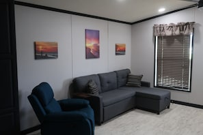 Ein modernes Wohnzimmer mit einer Eckcouch, einem blauen Sessel und drei an der Wand befestigten Bildern.