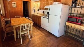 Eine Küche mit Holzausstattung, einem weißen Kühlschrank, einer Mikrowelle und einem Esstisch mit Stühlen.