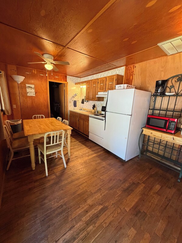 Une cuisine avec des meubles de rangement en bois, un réfrigérateur blanc, un four à micro-ondes et une table à manger avec des chaises.