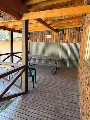 Un espace extérieur abrité, doté de tables et de chaises de pique-nique, de poutres en bois et d’un mur en métal ondulé.