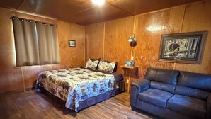 Ein Zimmer mit Holzboden, einem Bett mit gemustertem Überwurf, einem blauen Sofa, einer Lampe und einem gerahmten Bild an der Wand.