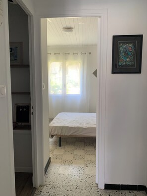 Un dormitorio con cama, ventana y puerta que da a otra habitación.
