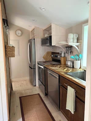 Eine moderne Küche mit Edelstahl-Kühlschrank, Mikrowelle und Backofen, Holzschränken, einer eingebauten Spüle und einem Fenster.