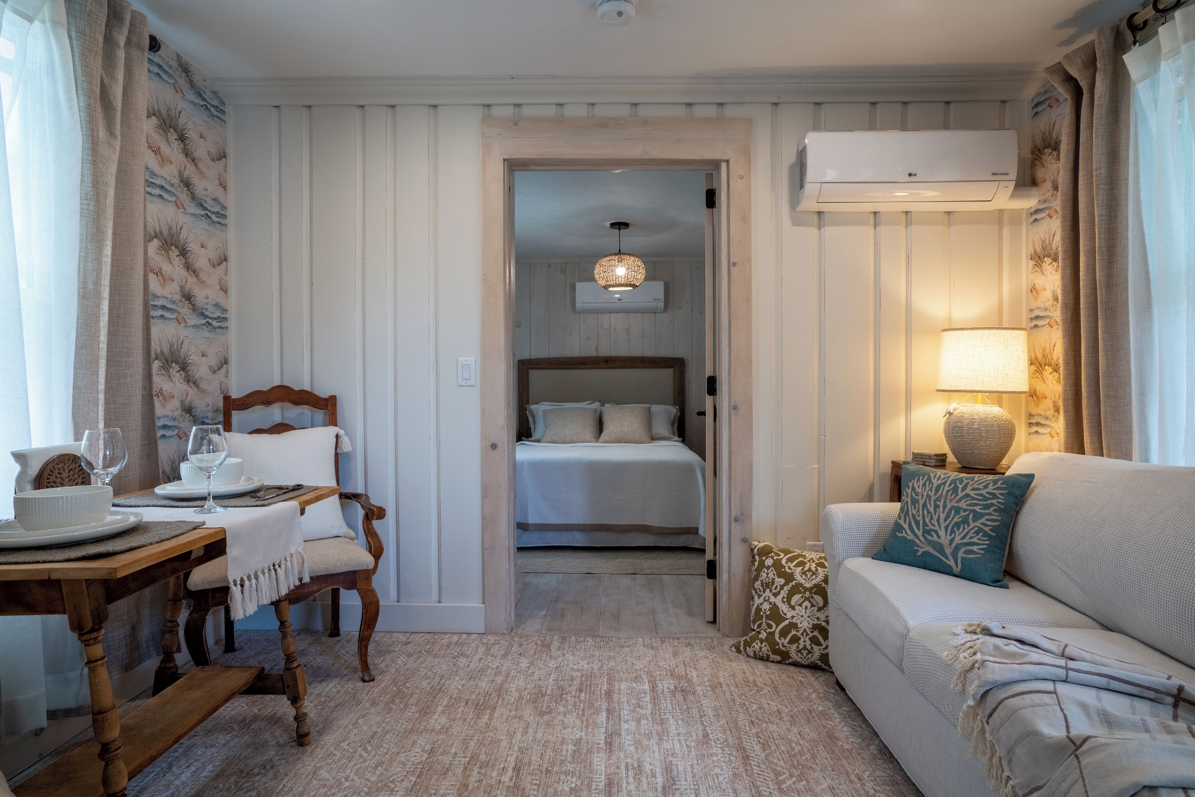 Une chambre d’hôtel comprenant une table à manger en bois, un canapé, un lit avec une tête de lit et un climatiseur fixé au mur.