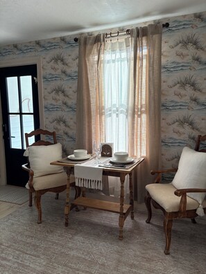 Ein Essbereich mit einem für zwei Personen gedeckten Tisch, zwei Holzstühlen, einer schwarzen Tür und einer Wand mit maritimem Wandpapier.