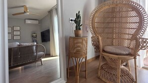 Ett rum med en stor spegel, en fåtölj i rotting, ett litet bord med en växt och en soffa.