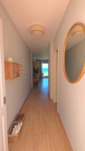 A hallway with a wooden floor, a mirror on the right, and a view of the outdoors. - Sunny apartment in the naturist area of Vera Playa with sea view (Playas de Vera)