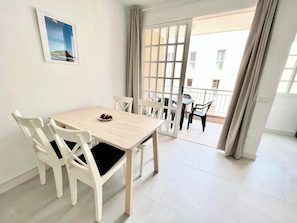 Ein Essbereich mit Holztisch und weißen Stühlen, ein Balkon mit Blick und ein gerahmtes Bild an der Wand.