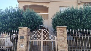 Un edificio de dos plantas con entrada protegida por una reja, pilares de piedra y un balcón.