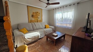 Una sala de estar con un sofá, una mesa de centro, un cuadro, una ventana con cortinas y un ventilador de techo.