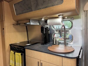 Eine kompakte Küchenzeile mit Herd, Kaffeemaschine und kleinem Fenster.