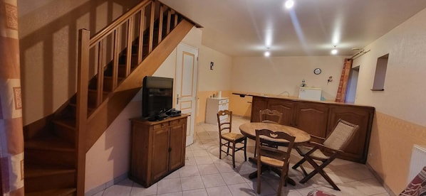 A dining area with a wooden table and chairs, a television on a cabinet, and a staircase.
