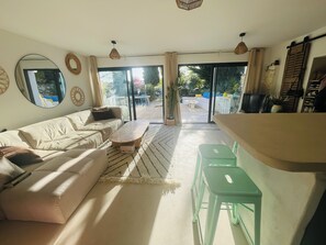 Una sala de estar con un sofá, una mesa de centro y un comedor con una mesa y sillas. Una ventana grande ofrece vistas al exterior.