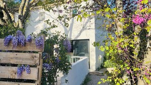 Een wit gebouw met een houten bank en paarse bloemen, omringd door groen.