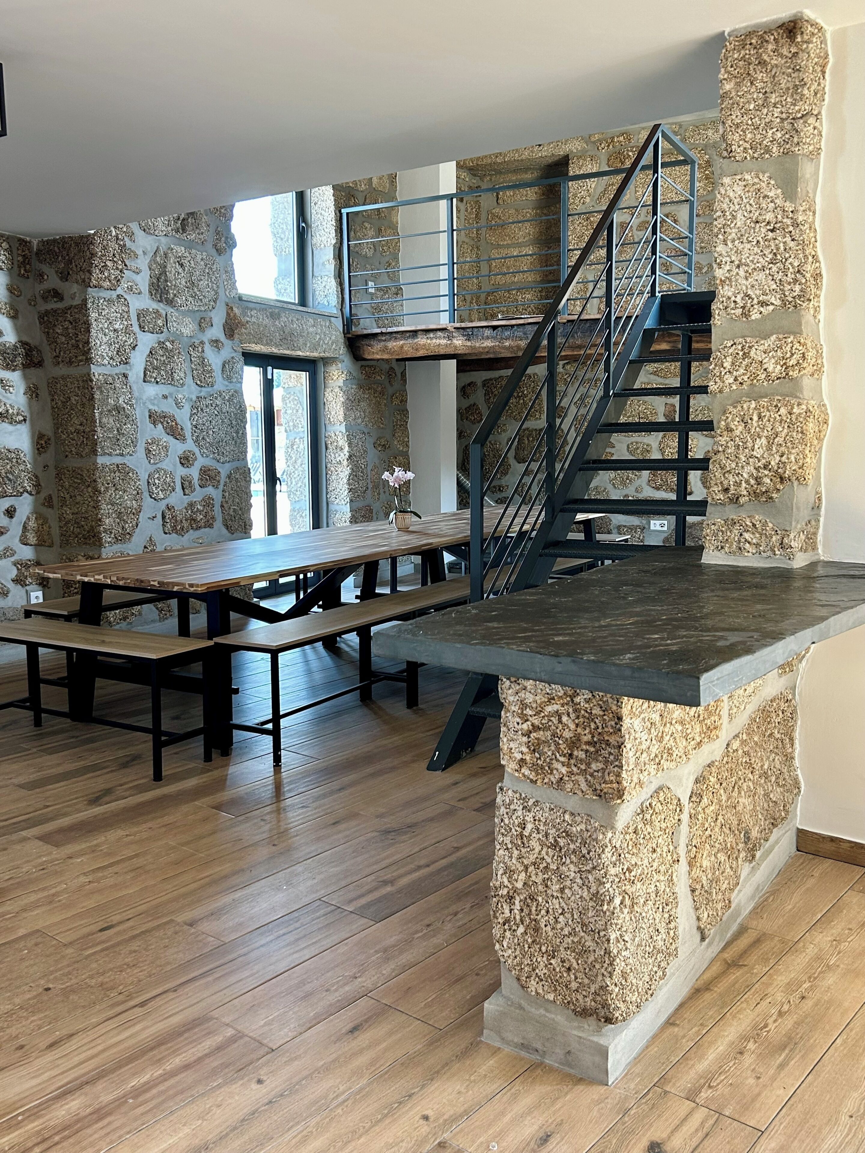 Une pièce spacieuse avec un mur en pierre, une table en bois, des bancs et un escalier.