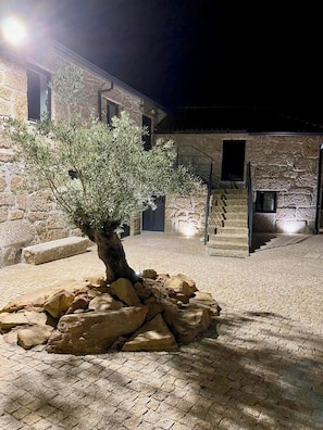 A stone building with a staircase, a tree, and a paved courtyard at night.