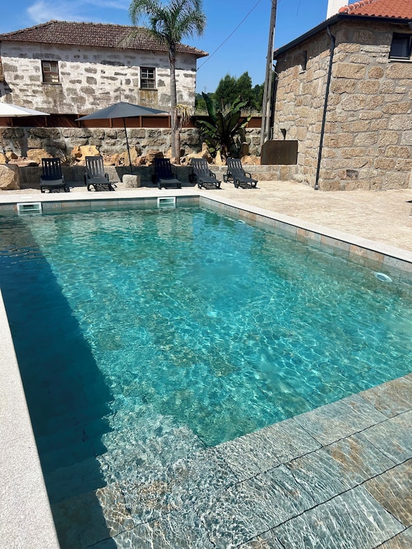Une piscine aux eaux cristallines, avec des chaises longues et des bâtiments en pierre en arrière-plan.