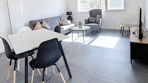Ein modernes Wohnzimmer mit Essbereich, Holzbalken, einer Couch, einem Couchtisch und einem Fernseher.